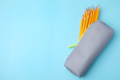 Many sharp pencils in pencil case on light blue background, top view. Space for text