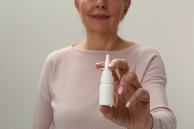 Photo of Woman holding nasal spray against light grey background, closeup
