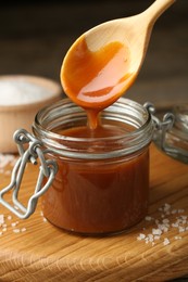 Photo of Taking tasty salted caramel with spoon from jar on table, closeup