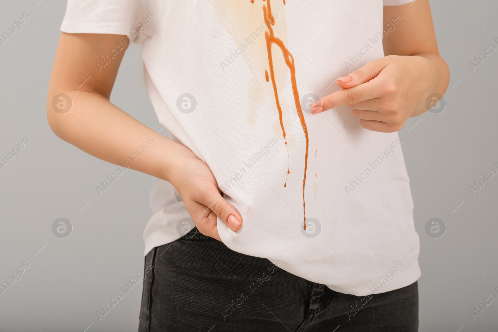 Photo of Woman showing stain from condensed milk on her shirt against light grey background, closeup