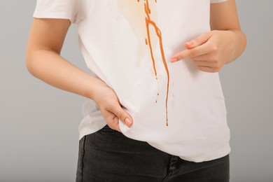 Woman showing stain from condensed milk on her shirt against light grey background, closeup