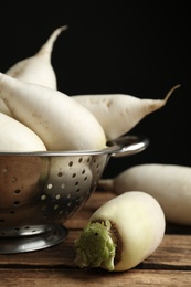 Photo of White turnips in colander on wooden table, closeup