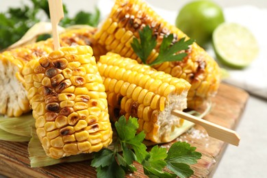 Photo of Tasty grilled corn cobs with parsley on wooden board, closeup