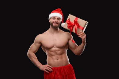 Attractive young man with muscular body holding Christmas gift box on black background