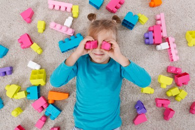 Cute little girl playing with colorful building blocks on floor, top view