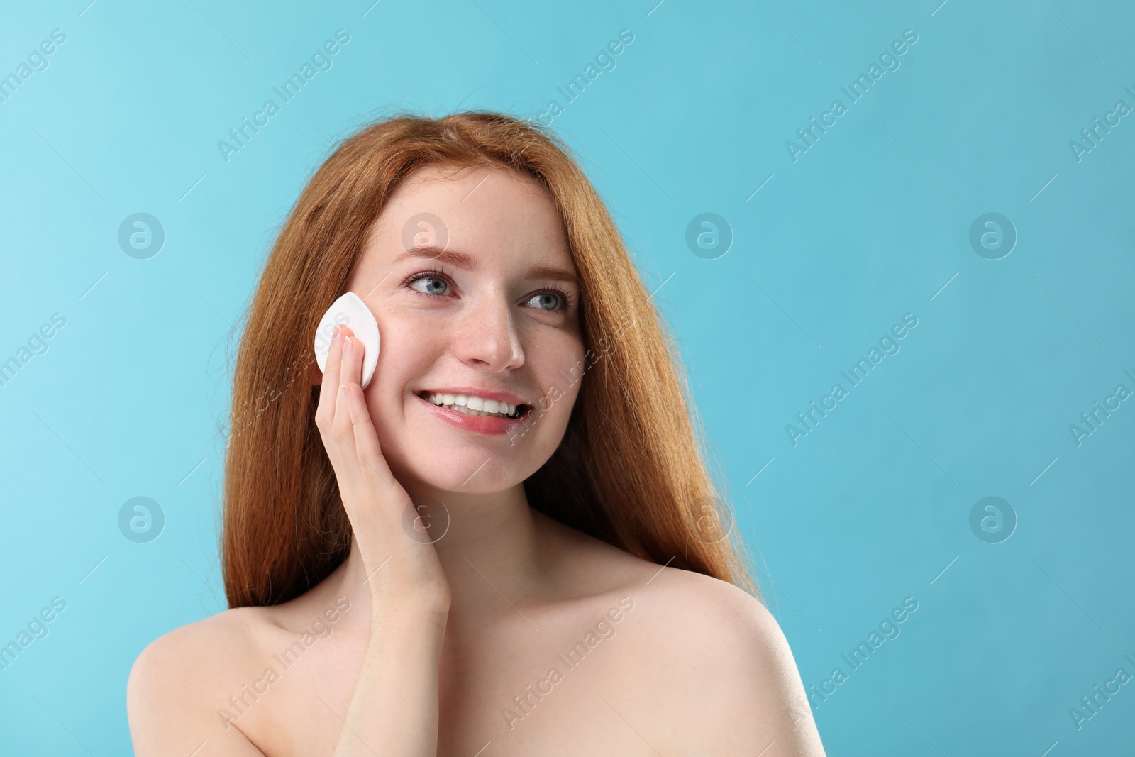 Photo of Smiling woman with freckles wiping face on light blue background. Space for text