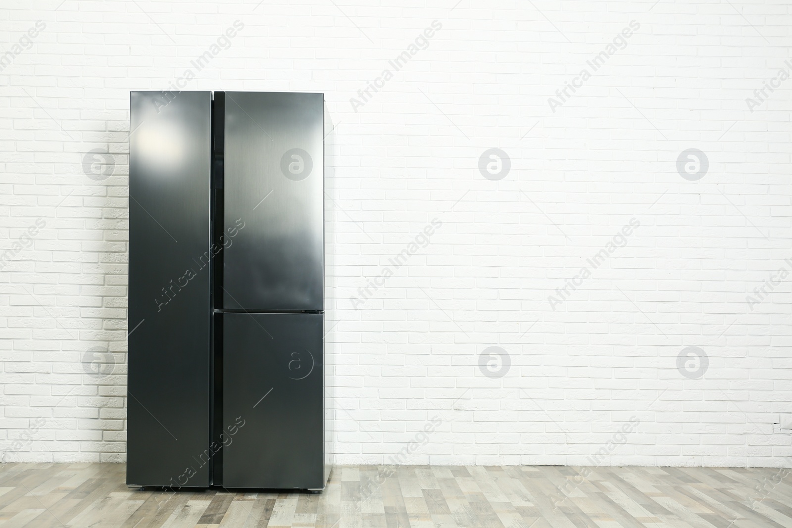 Photo of Modern refrigerator near white brick wall, space for text