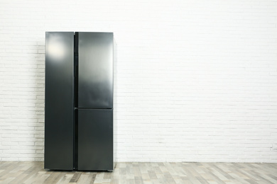 Photo of Modern refrigerator near white brick wall, space for text