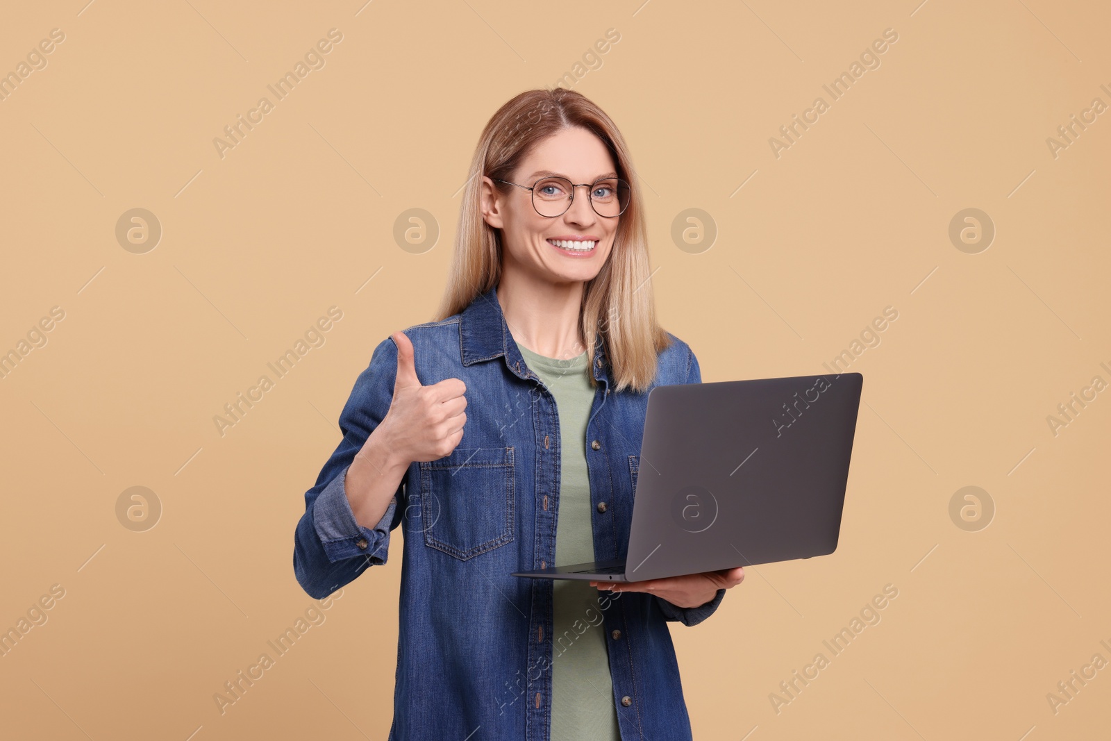 Photo of Happy woman with laptop showing thumb up on beige background