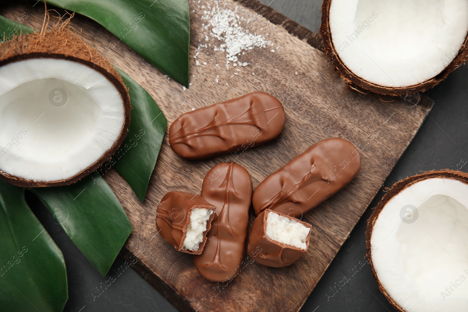 Photo of Delicious milk chocolate candy bars with coconut filling on black table, flat lay