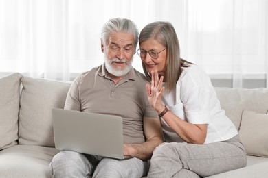 Senior couple using laptop on sofa at home
