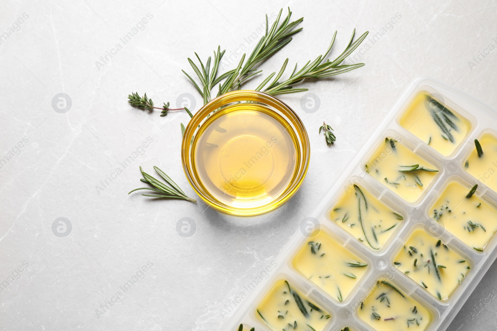 Photo of Ice cube tray with herbs frozen in oil and fresh rosemary on grey table, flat lay