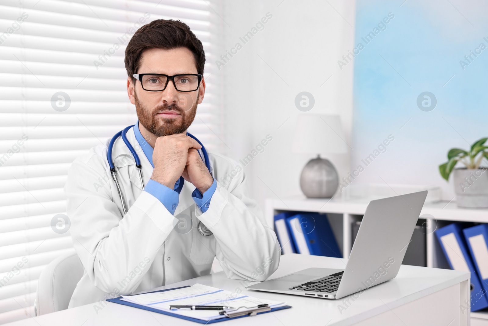 Photo of Medical consultant with glasses and stethoscope at table in clinic