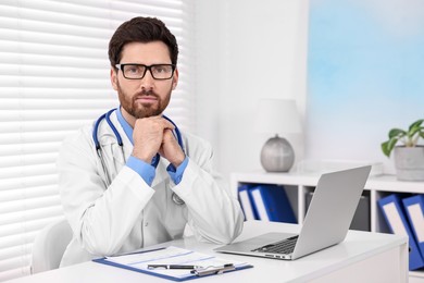 Medical consultant with glasses and stethoscope at table in clinic