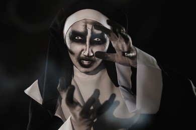 Photo of Portrait of scary devilish nun and smoke on black background. Halloween party look