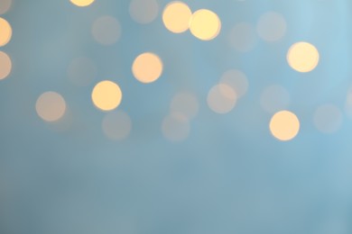 Blurred view of festive lights on light blue background. Bokeh effect