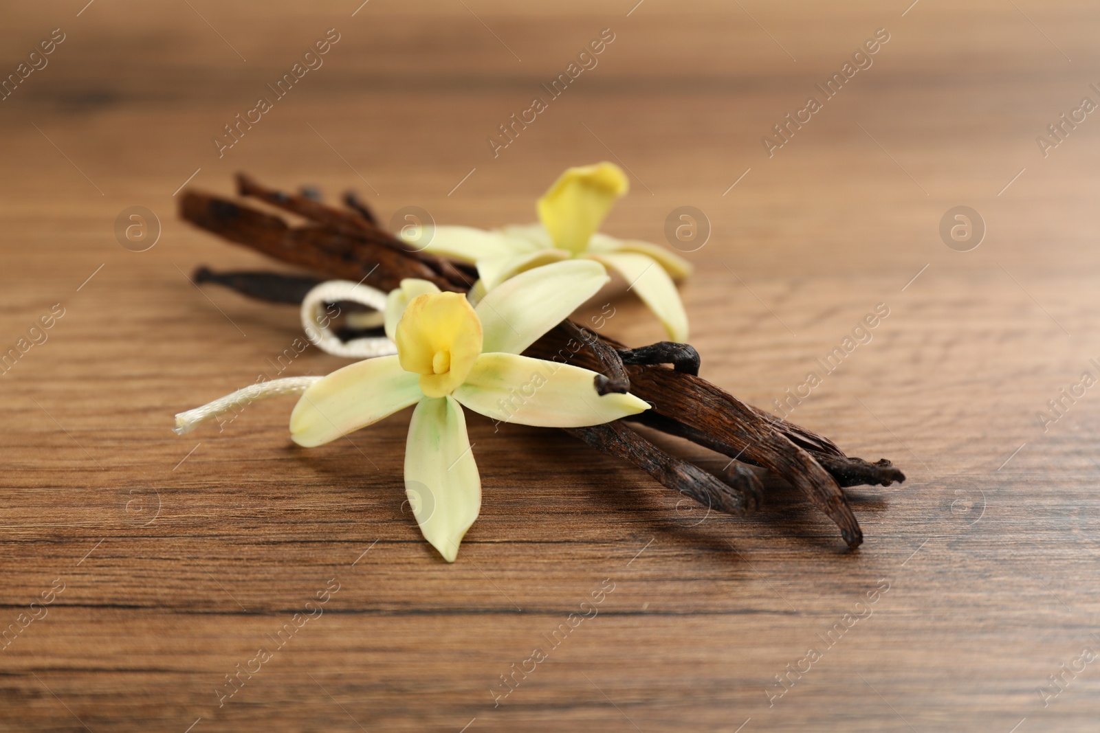 Photo of Aromatic vanilla sticks and flowers on wooden table, closeup