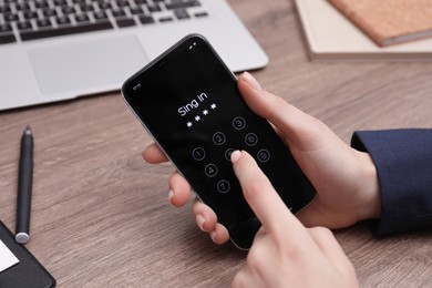 Photo of Woman unlocking smartphone with blocked screen at wooden table, closeup