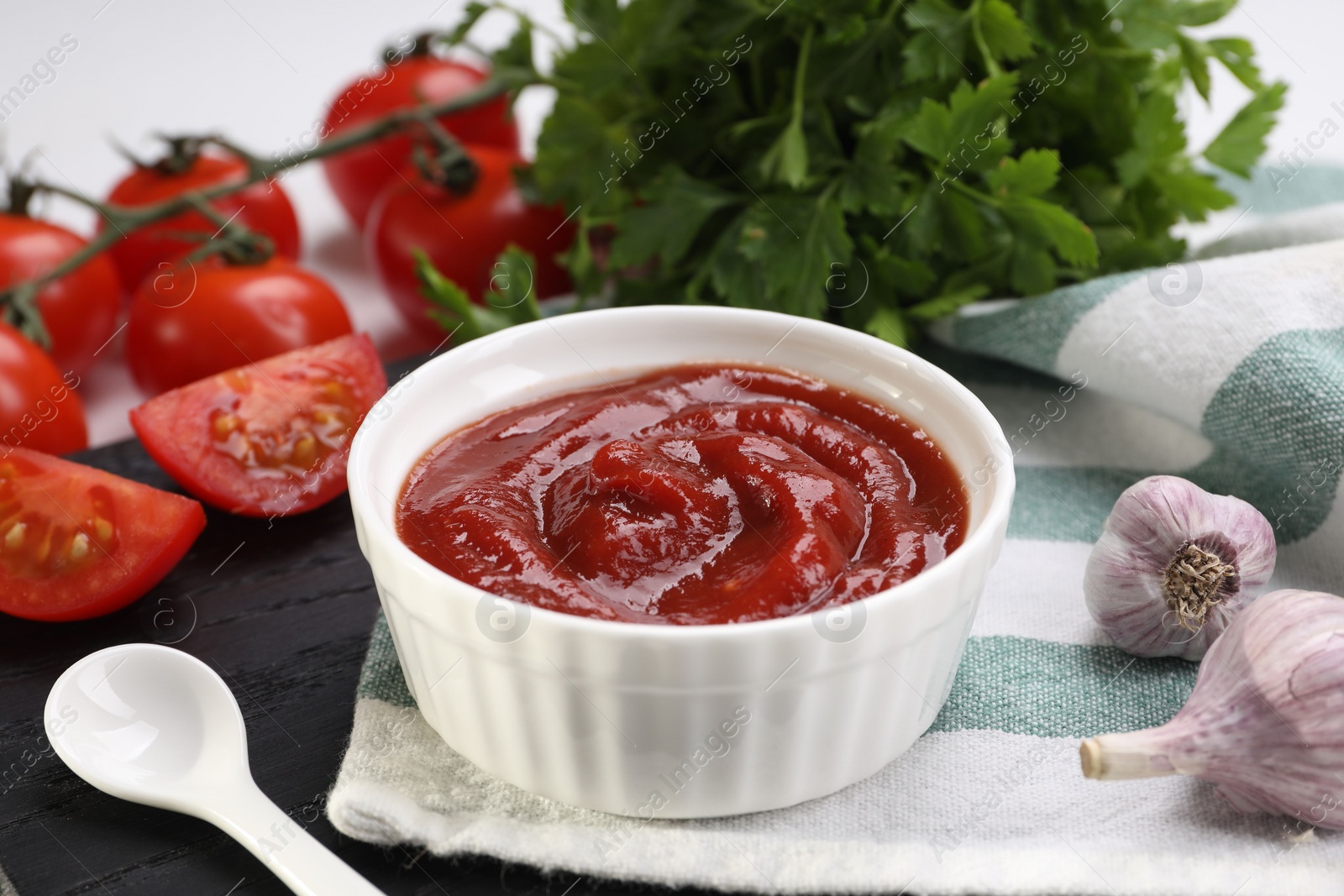 Photo of Organic ketchup in bowl, fresh tomatoes, parsley and garlic on table, closeup. Tomato sauce