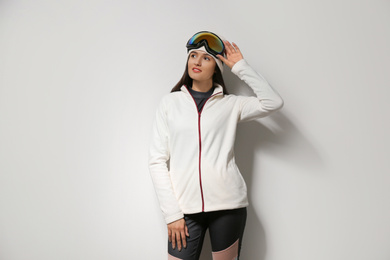 Photo of Woman wearing fleece jacket and goggles on light grey background. Winter sport clothes