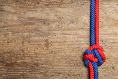 Top view of colorful ropes tied together on wooden background, space for text. Unity concept