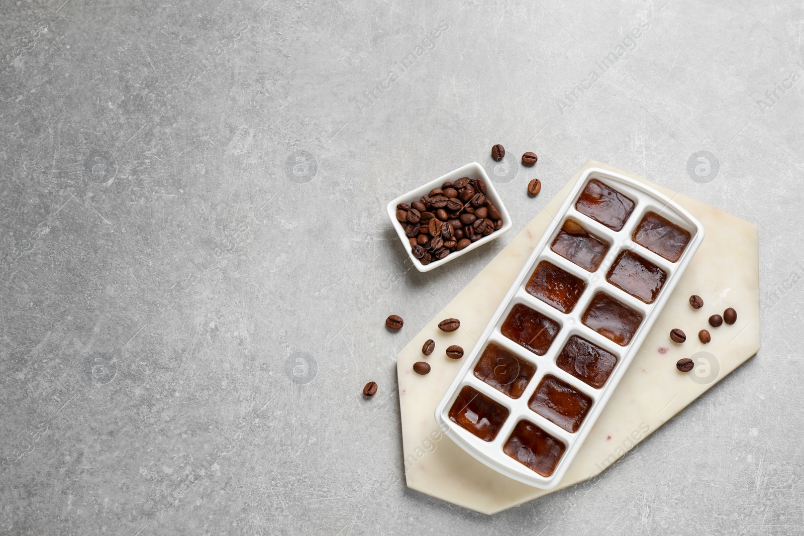 Photo of Ice cubes with coffee beans in tray on grey table, flat lay. Space for text