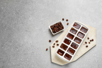 Ice cubes with coffee beans in tray on grey table, flat lay. Space for text