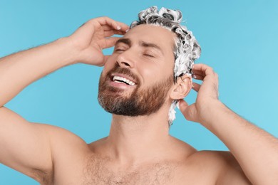 Happy man washing his hair with shampoo on light blue background, closeup