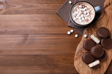 Photo of Tasty choco pies and cocoa with marshmallows on wooden table, flat lay. Space for text