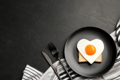Photo of Tasty fried egg in shape of heart with toast served on black table, flat lay. Space for text