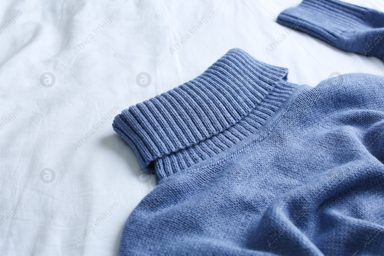 Photo of Blue warm sweater on white crumpled fabric, closeup