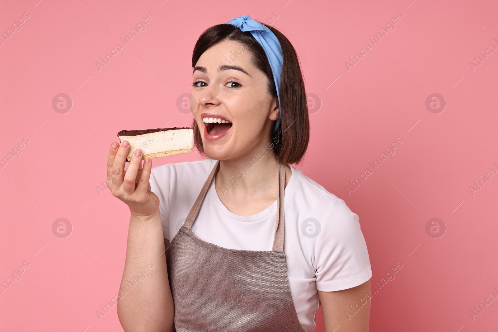 Photo of Happy confectioner eating cheesecake on pink background