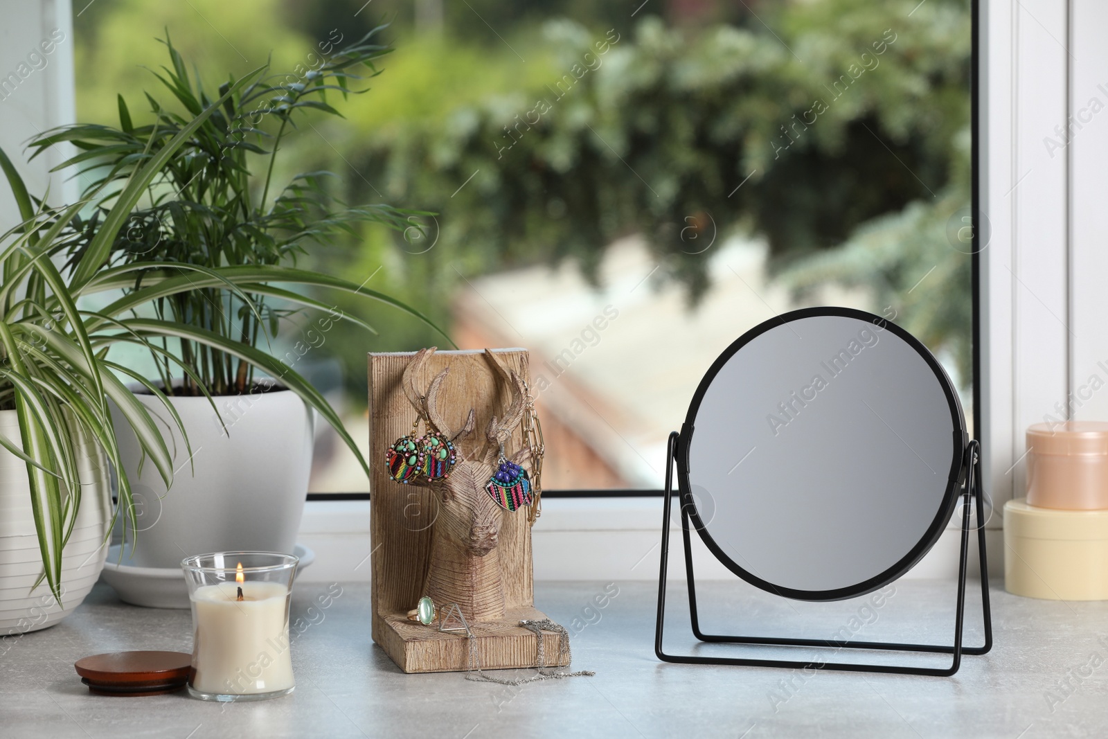 Photo of Mirror, jewelry, candles and houseplants on light grey stone window sill