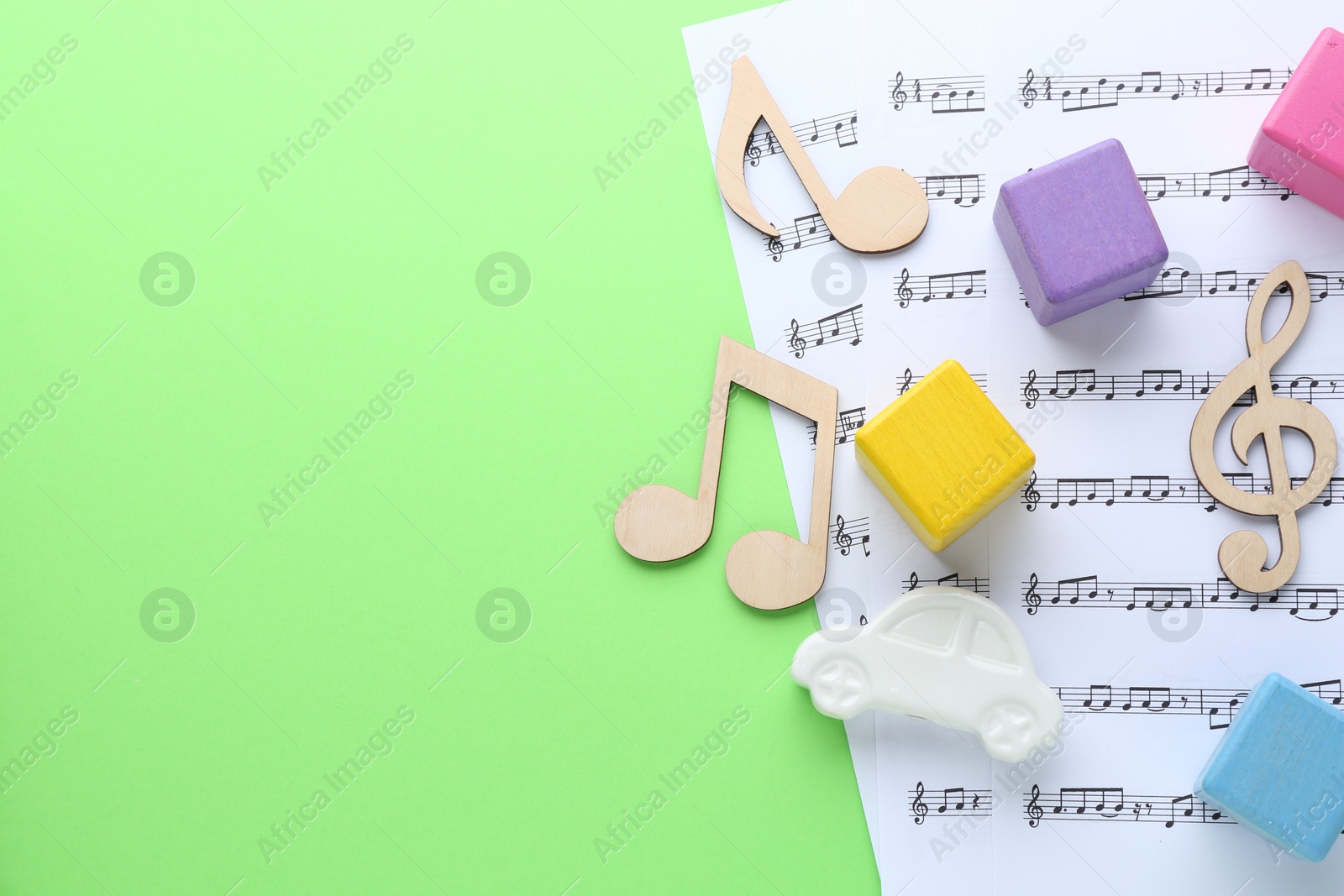 Photo of Wooden notes, music sheets and toys on light green background, top view with space for text. Baby song concept