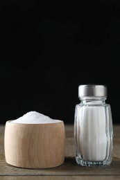 Photo of Organic salt in bowl and glass shaker on wooden table, closeup. Space for text