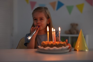 Photo of Birthday celebration. Cute girl holding blower at table with tasty cake indoors