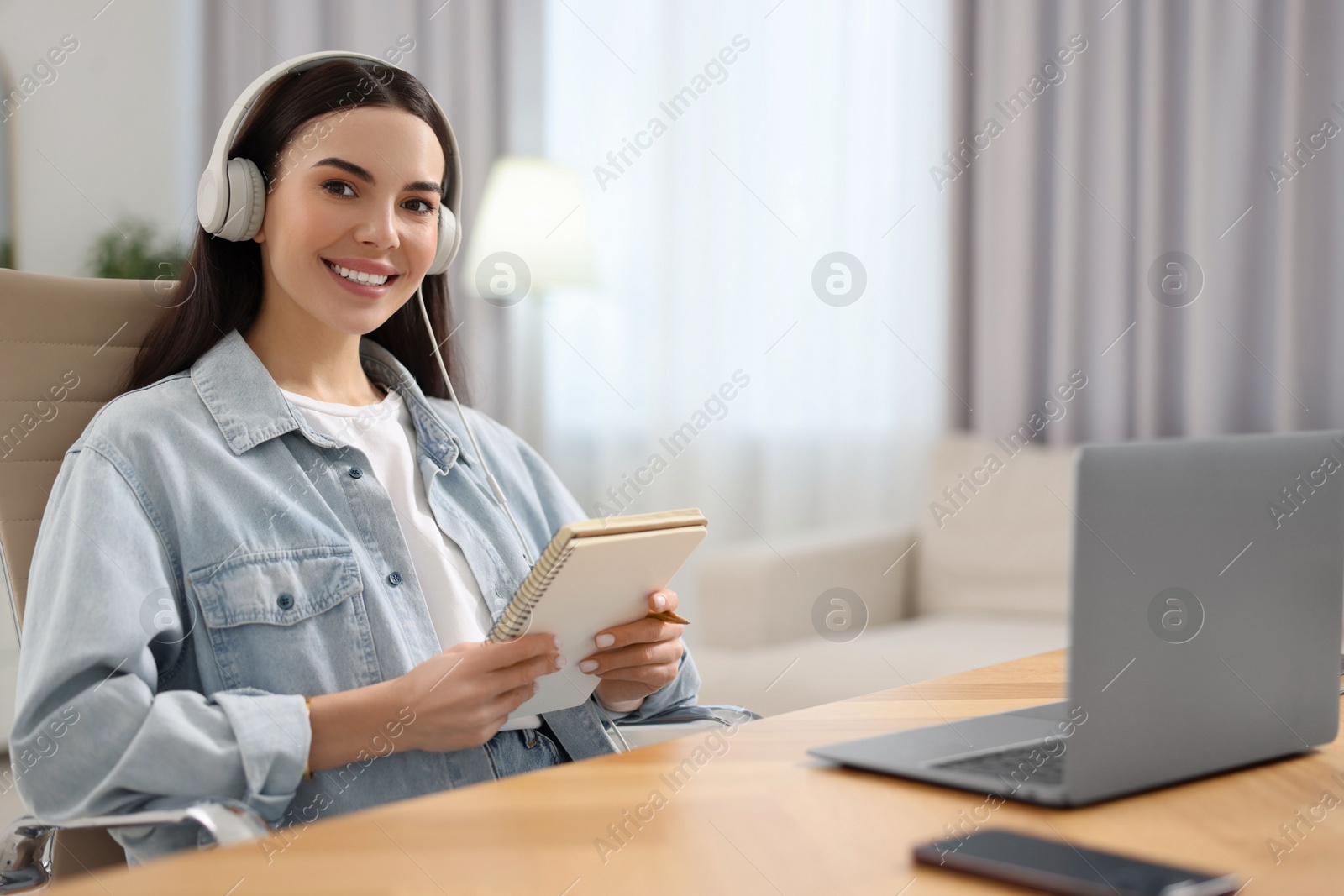 Photo of Young woman in headphones watching webinar at table in room