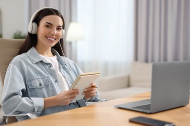 Photo of Young woman in headphones watching webinar at table in room