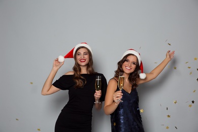 Happy women in Santa hats with champagne on grey background. Christmas party