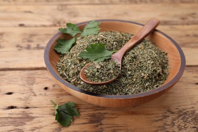 Bowl and spoon with dried parsley on wooden table, closeup