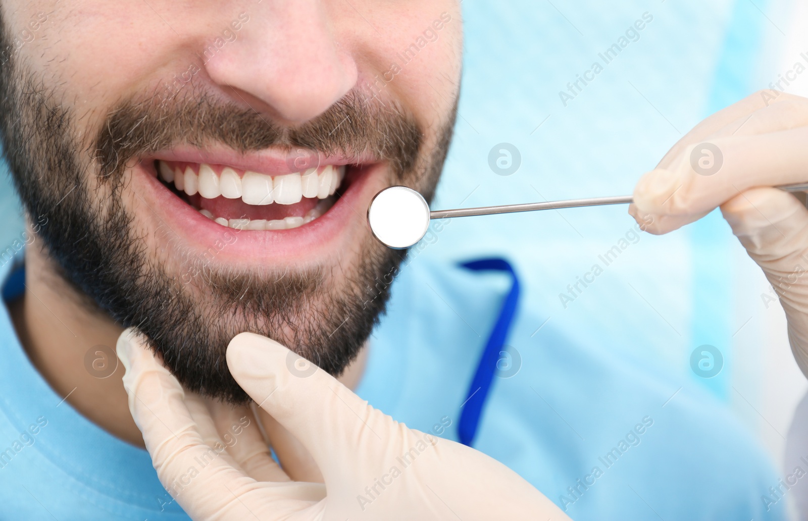 Photo of Dentist examining young man's teeth with mirror, closeup