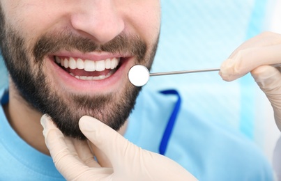 Photo of Dentist examining young man's teeth with mirror, closeup