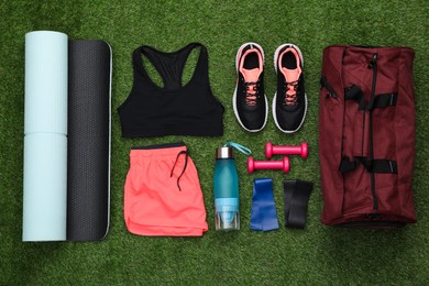 Photo of Gym bag and sports equipment on green grass, flat lay
