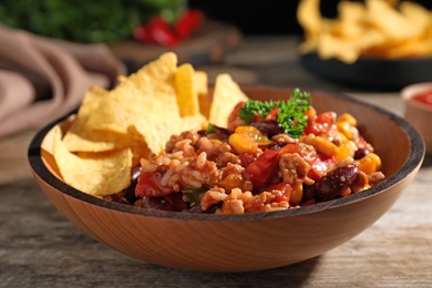 Photo of Tasty chili con carne served with tortilla chips in bowl on table