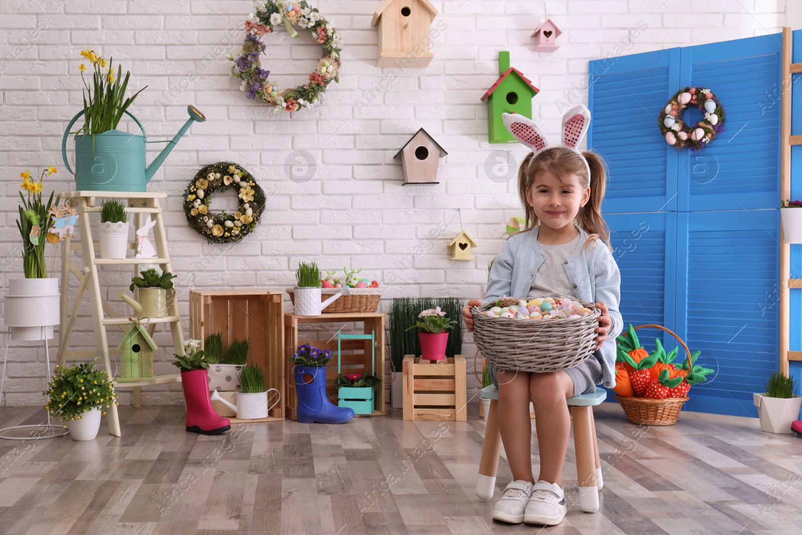 Photo of Adorable little girl with bunny ears and basket full of dyed eggs in Easter photo zone