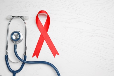 Red ribbon and stethoscope on white wooden background, flat lay with space for text. AIDS disease awareness