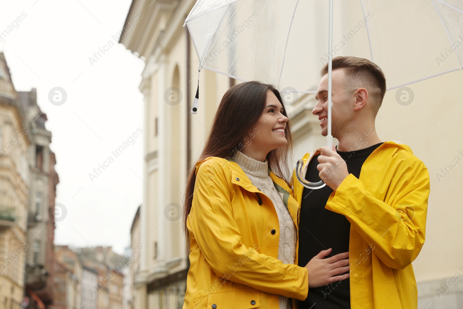 Photo of Lovely young couple with umbrella walking under rain on city street