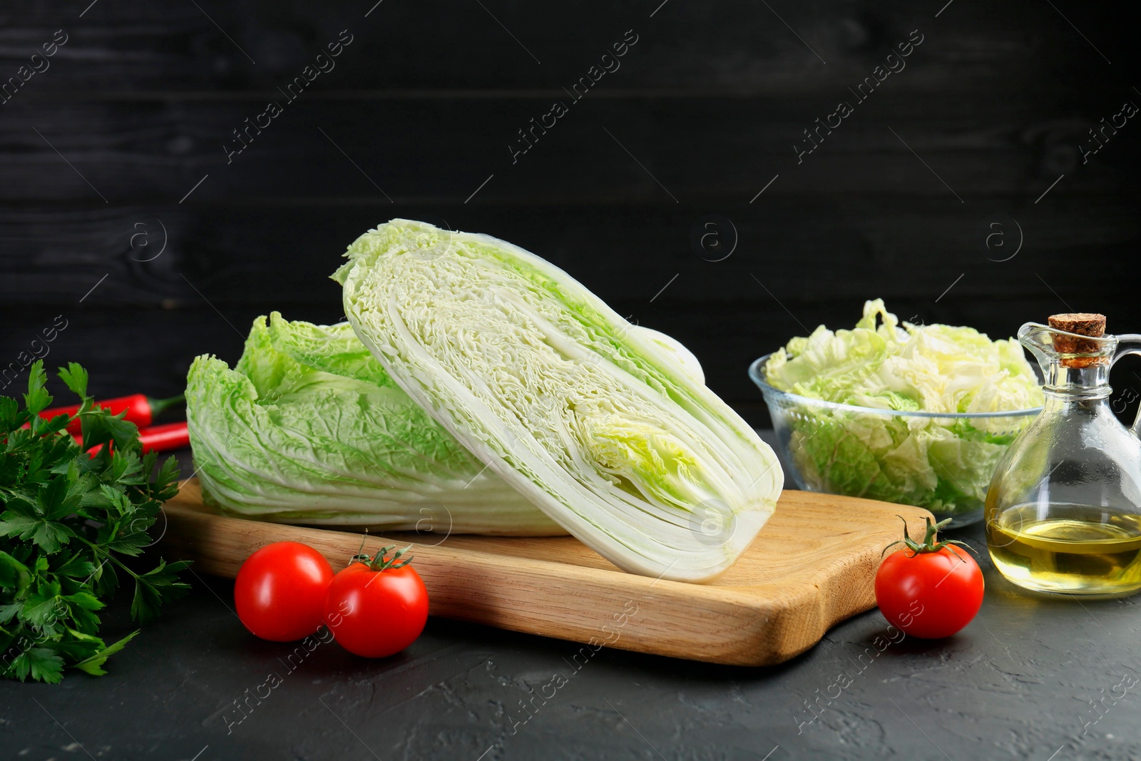 Photo of Fresh Chinese cabbages, tomatoes, parsley and oil on black textured table