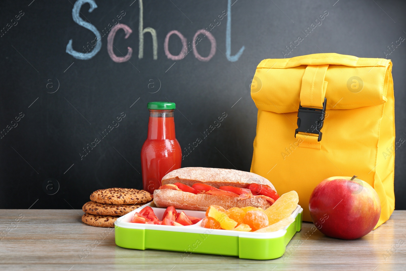 Photo of Appetizing food in lunch box and bag on table near chalkboard with word SCHOOL