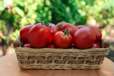 Photo of Wicker basket with fresh tomatoes on wooden table outdoors